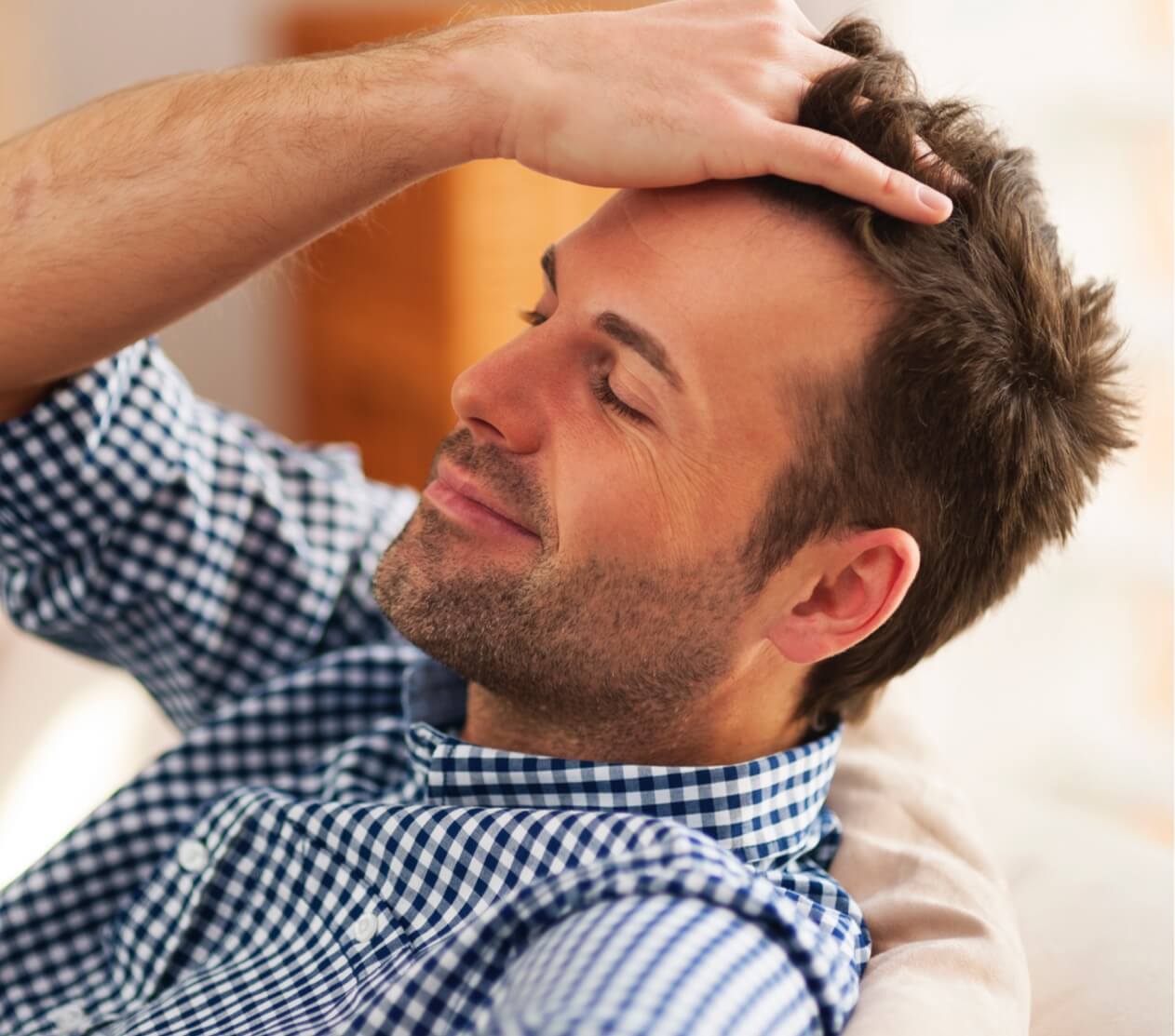 Man smiling while running fingers thru his hair enjoying the benefits of hair restoration services.