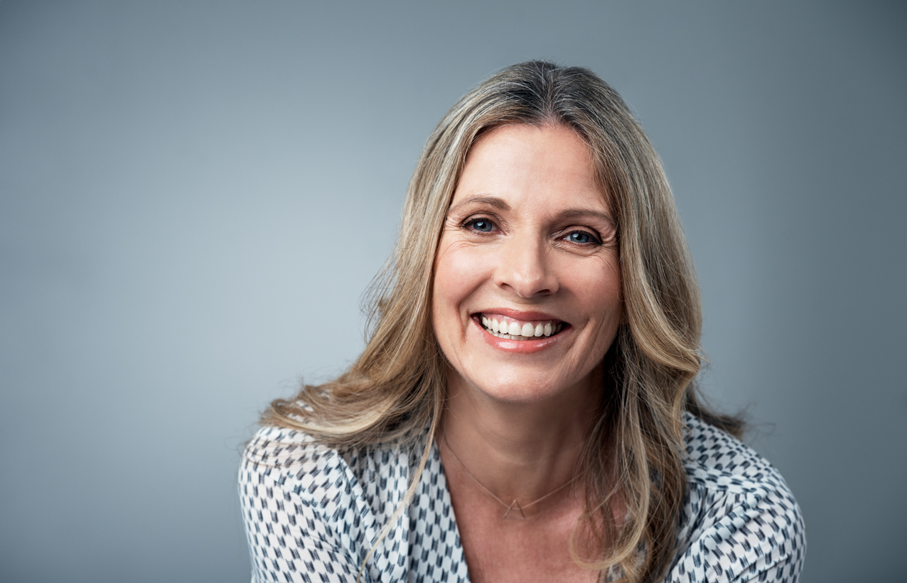 Her confidence just shines Middle-aged blonde woman smiles for a portrait on a blue background.